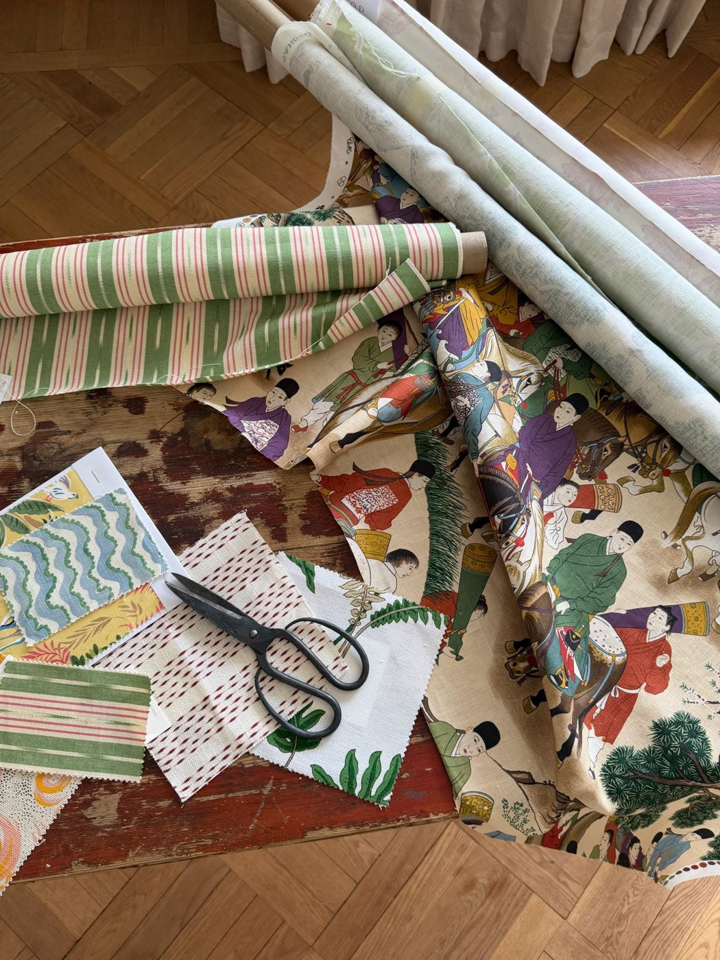 Rolls of printed fabric, swatches and a pair of scissors on the atelier floor