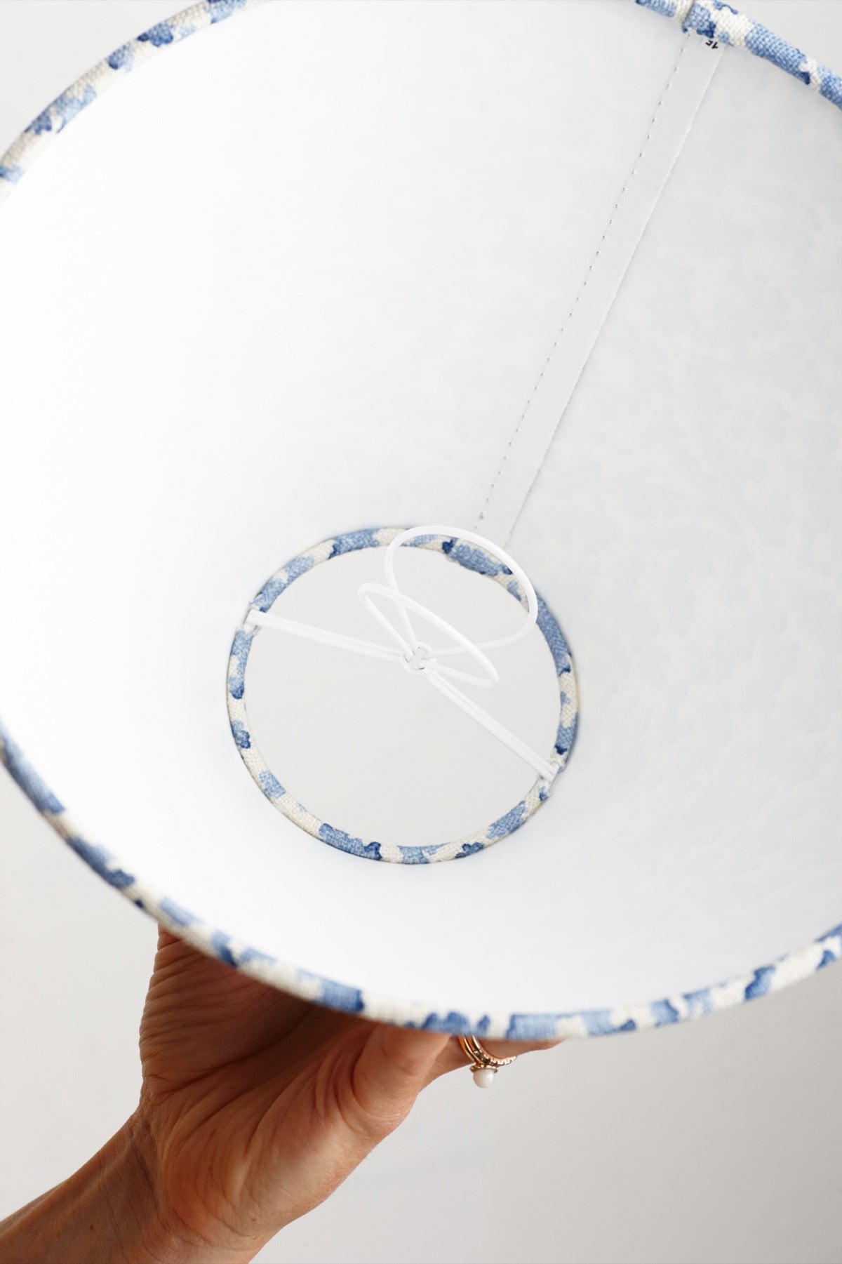 A hand holding a lampshade up and seen from below, showing the blue trimmed ring and the wire fitting inside it