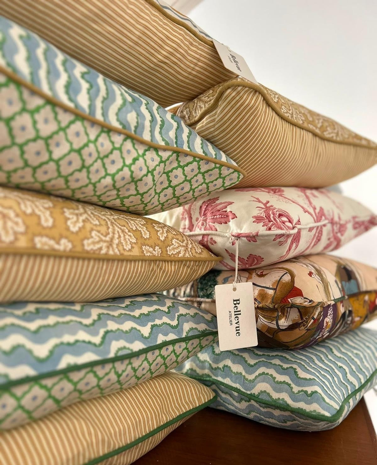 A stack of cushions in printed cottons with a Bellevue Atelier tag, on a wooden table